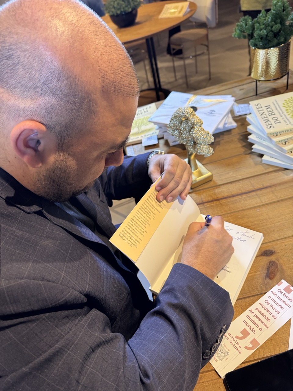 Junior A Rocha assinando livro com marcador e pilha de exemplares ao fundo