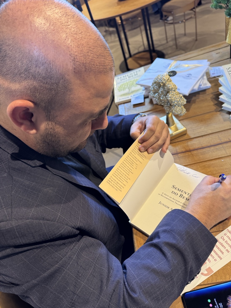 Junior assinando a página de título do livro Sementes do Bem